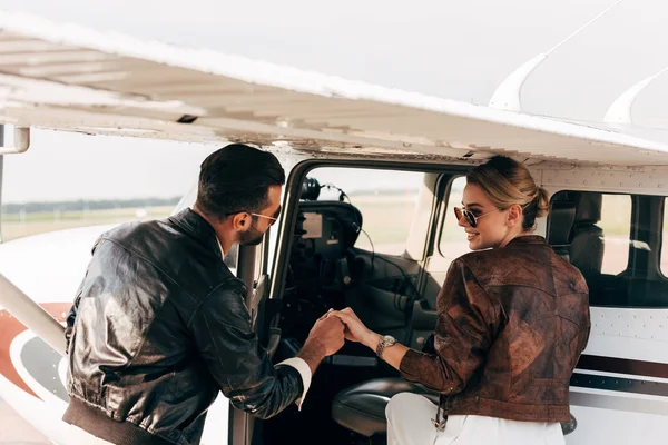 Junger Mann in Lederjacke hilft Freundin beim Einsteigen in Flugzeug — Stockfoto