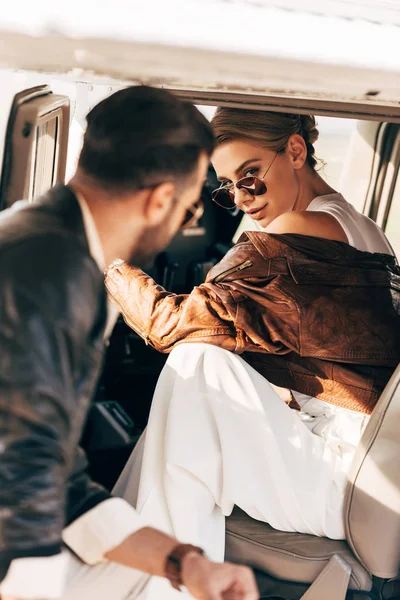 Enfoque selectivo de mujer atractiva en gafas de sol sentado en el avión mientras su novio de pie cerca — Stock Photo