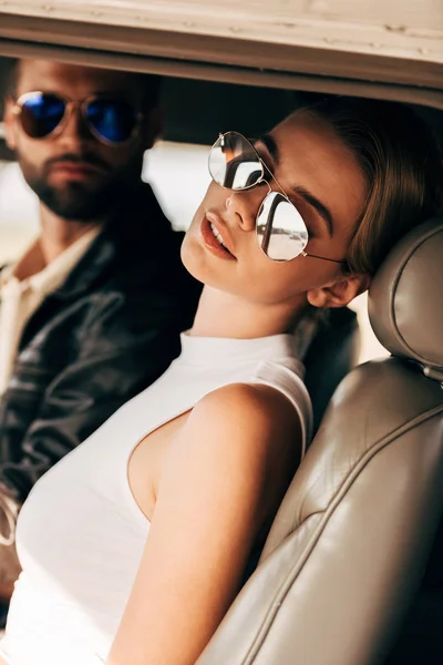 Selective focus of beautiful young woman in sunglasses sitting near male pilot in cabin of airplane — Stock Photo