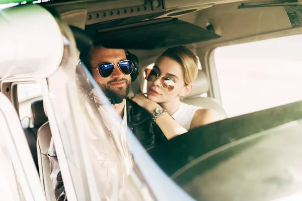 Молодий чоловік-пілот в гарнітурі і сонцезахисних окулярах сидить з дівчиною в салоні літака — стокове фото