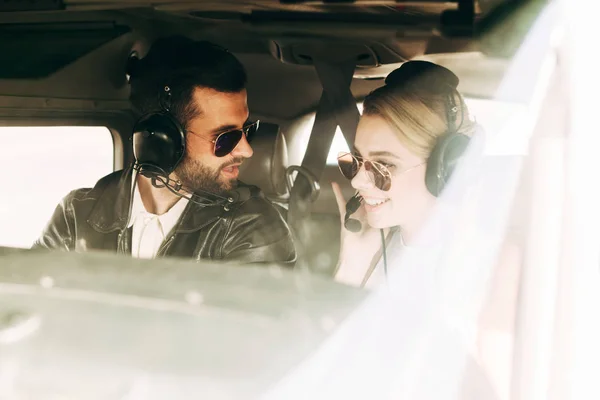 Male pilot in headset and sunglasses talking to girlfriend in cabin of airplane — Stock Photo