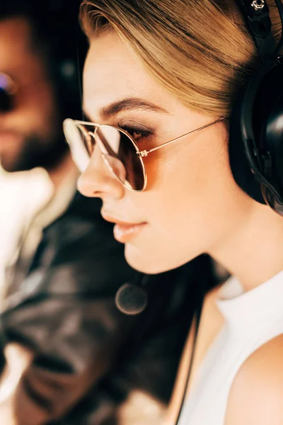 Selective focus of beautiful woman in sunglasses and headset sitting near male pilot in cabin of airplane — Stock Photo