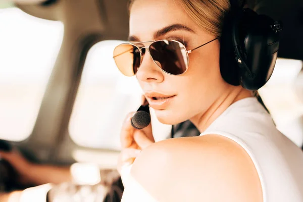 Крупным планом портрет привлекательной женщины в солнечных очках с наушниками, смотрящей в камеру в самолете — стоковое фото