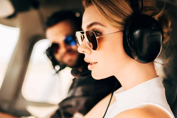 Side view of attractive woman in sunglasses and headset sitting near male pilot in cabin of airplane — Stock Photo