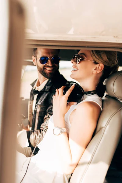 Happy male pilot in sunglasses sitting with girlfriend in cabin of airplane — Stock Photo