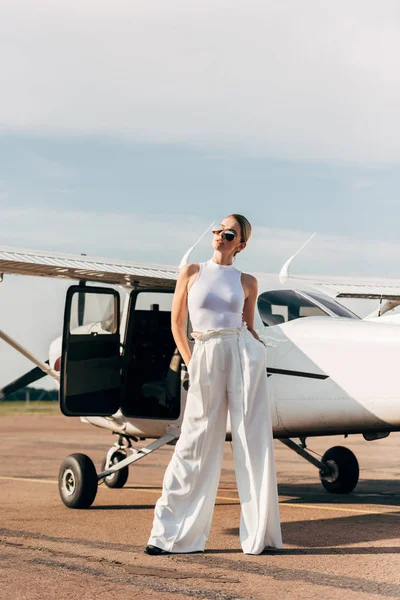 Fashionable young woman in sunglasses posing near plane — Stock Photo