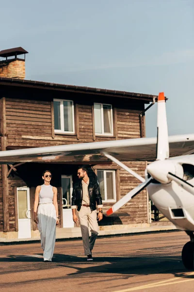 Junge Frau spaziert mit Freund in Lederjacke in der Nähe von Flugzeug — Stockfoto