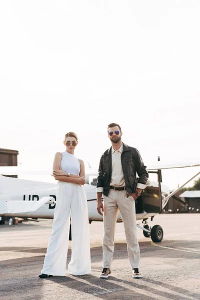 Молода модна пара в сонцезахисних окулярах позує біля літака — стокове фото