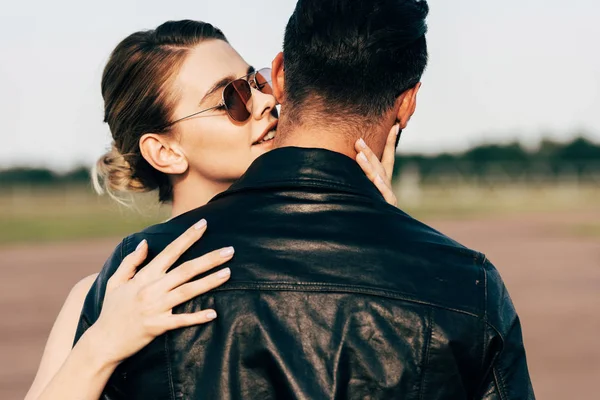 Selective focus of beautiful smiling woman embracing boyfriend in leather jacket — Stock Photo