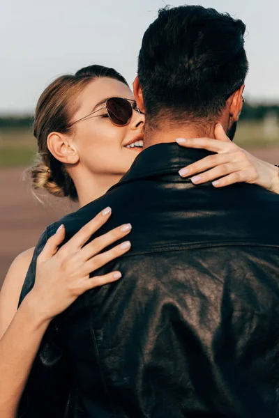 Mujer atractiva sonriente abrazando novio en chaqueta de cuero - foto de stock