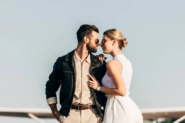 Vue latérale du jeune couple élégant en lunettes de soleil debout face à face — Photo de stock