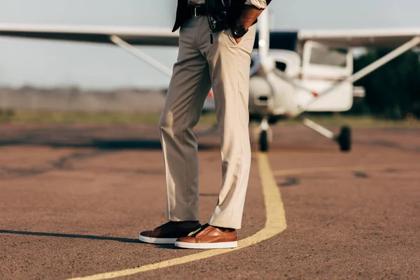 Imagem cortada de homem elegante em calças e tênis perto de avião — Fotografia de Stock