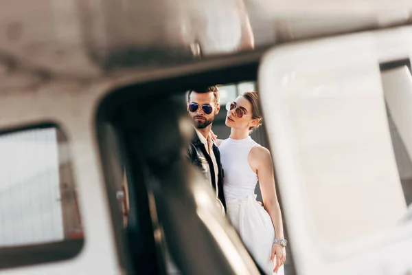 Enfoque selectivo de hombre guapo en chaqueta de cuero y gafas de sol de pie con novia cerca de avión - foto de stock