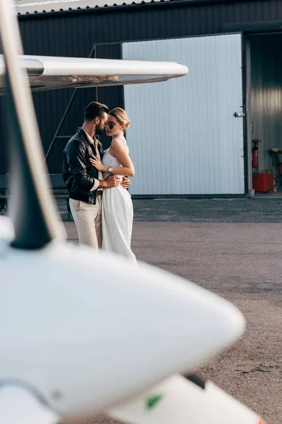 Mann in Lederjacke und Sonnenbrille umarmt attraktive Freundin in Flugzeugnähe — Stockfoto