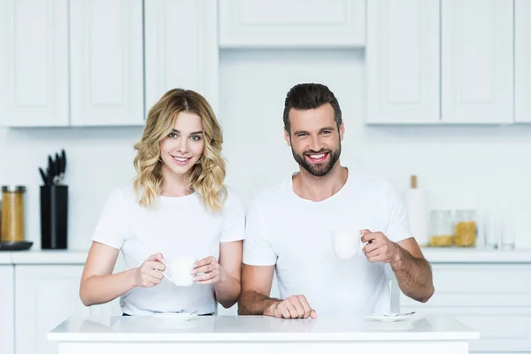 Glückliches junges Paar hält Tassen Kaffee in der Hand und lächelt in die Kamera — Stockfoto