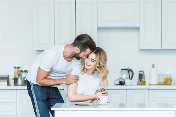 Feliz joven pareja abrazando durante el desayuno en la cocina - foto de stock