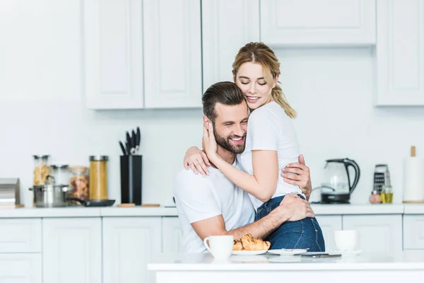 Beau jeune couple heureux dans l'amour câlins pendant le petit déjeuner dans la cuisine — Photo de stock