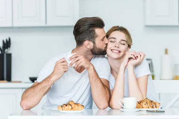 Beau jeune homme embrassant petit déjeuner heureux tout en prenant le petit déjeuner ensemble — Photo de stock