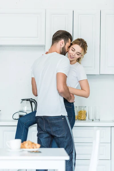 Bonito jovem homem abraçando atraente sorrindo namorada na cozinha — Fotografia de Stock