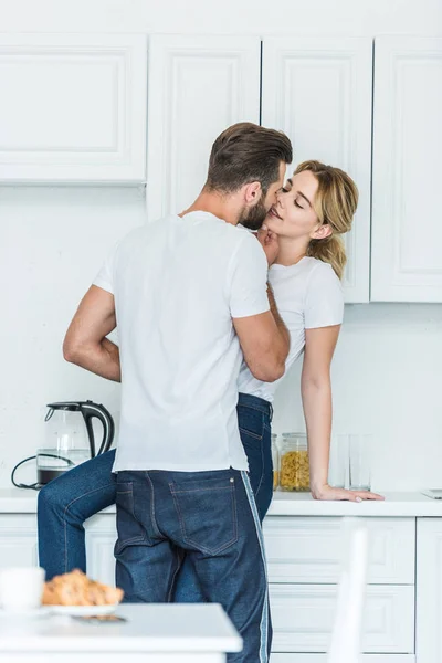 Beautiful happy young couple in love kissing at kitchen — Stock Photo