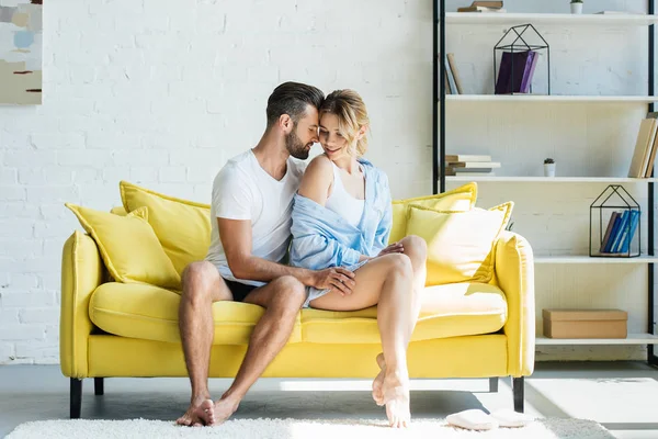 Ganzkörperansicht des jungen Barfußpaares in Unterwäsche, das zusammen auf der gelben Couch sitzt — Stockfoto