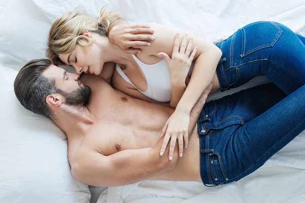 Вид на соблазнительную молодую пару в джинсах, обнимающую и лежащую вместе на кровати — стоковое фото