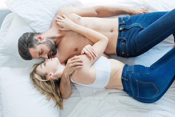 Top view of beautiful seductive young couple hugging and lying together on bed — Stock Photo