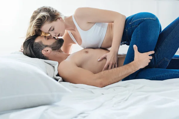 Vue latérale d'un jeune couple passionné embrassant et embrassant au lit — Photo de stock
