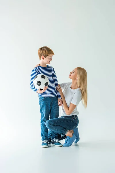 Mother squatting near son with football ball on white — Stock Photo