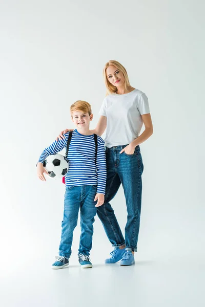 Mãe alegre e filho de pé com bola de futebol no branco e olhando para a câmera — Fotografia de Stock