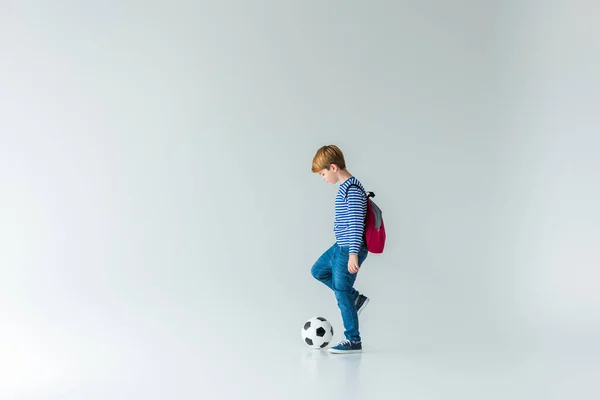 Vista lateral de estudante adorável com mochila jogando com bola de fotball no branco — Fotografia de Stock