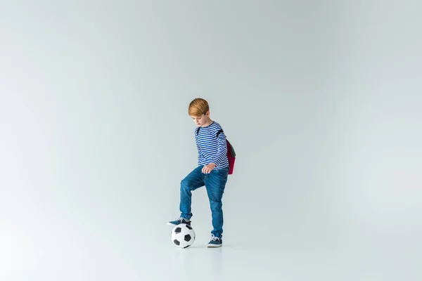 Entzückender Schuljunge mit Rucksack, der Bein auf Ball auf Weiß setzt — Stockfoto