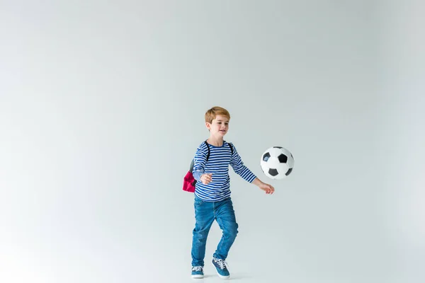 Adorável estudante com mochila jogando com bola de fotball no branco — Fotografia de Stock