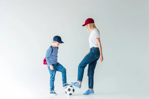 Vista laterale di madre e figlio in camicie e jeans che giocano a calcio su bianco — Foto stock