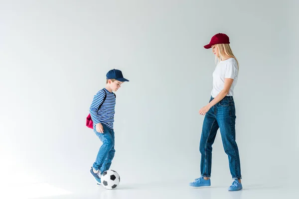 Seitenansicht von Mutter und Sohn mit Rucksack, der mit Fußball auf Weiß spielt — Stockfoto