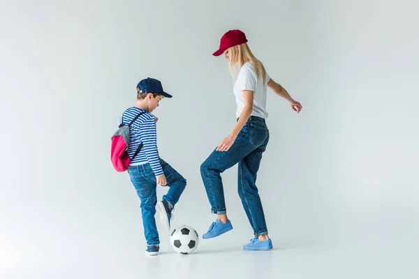 Vista laterale di madre e figlio in abiti casual giocare a calcio su bianco — Foto stock