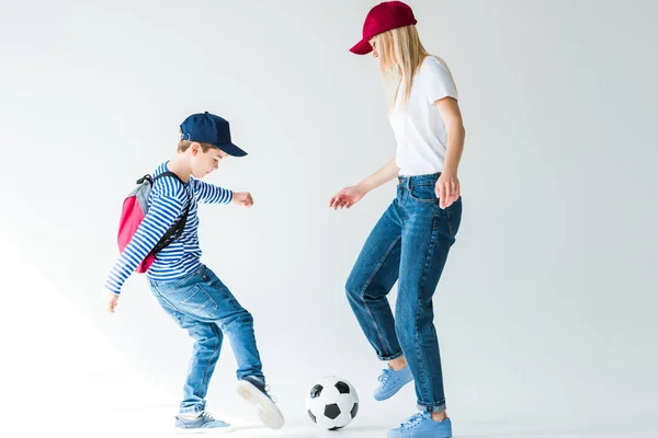 Vista lateral da mamãe e filho com mochila jogando futebol no branco — Fotografia de Stock