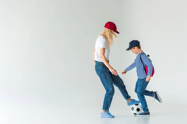 Vista lateral de mãe e filho com mochila jogando futebol no branco — Fotografia de Stock