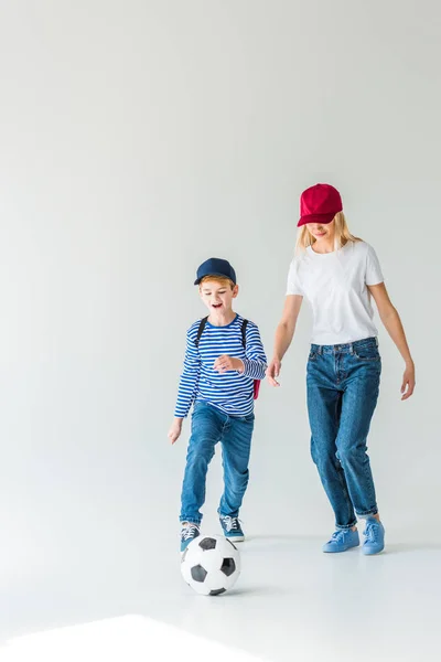 Mutter und Sohn mit Rucksack spielen gemeinsam Fußball auf weiß — Stockfoto