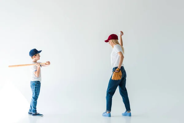 Vista lateral de la madre lanzando pelota de béisbol al hijo con bate de béisbol aislado en blanco - foto de stock