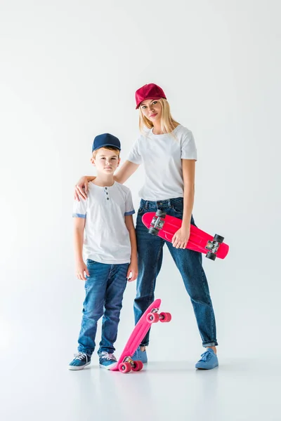 Mère et fils en casquettes debout avec des patins et regardant la caméra sur blanc — Photo de stock