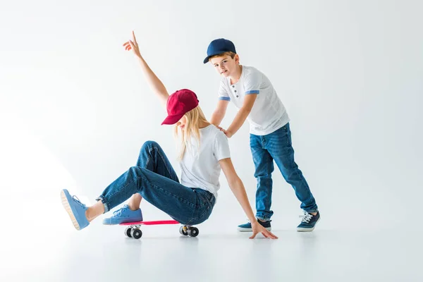 Filho empurrando mãe no skate no branco, ela mostrando uma mão para cima — Fotografia de Stock