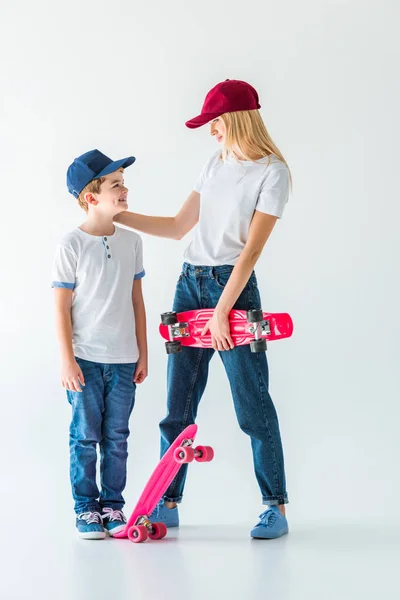 Madre e hijo en gorras de pie con patines y mirándose el uno al otro en blanco - foto de stock