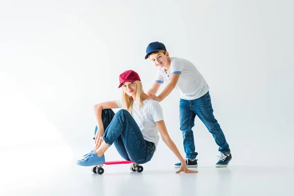 Feliz filho empurrando mãe no skate no branco — Fotografia de Stock