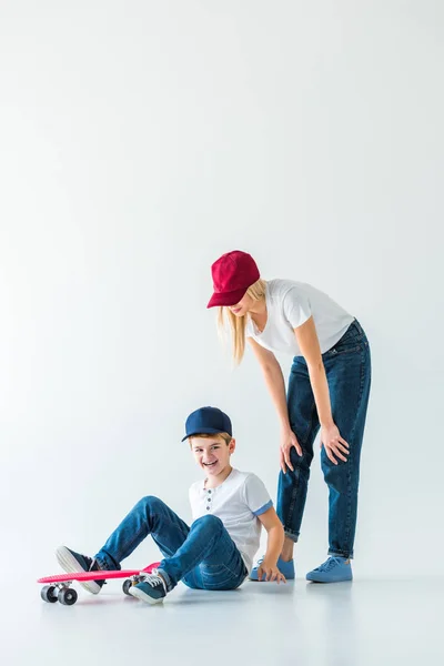 Mother looking at laughing son fell from skate on white — Stock Photo