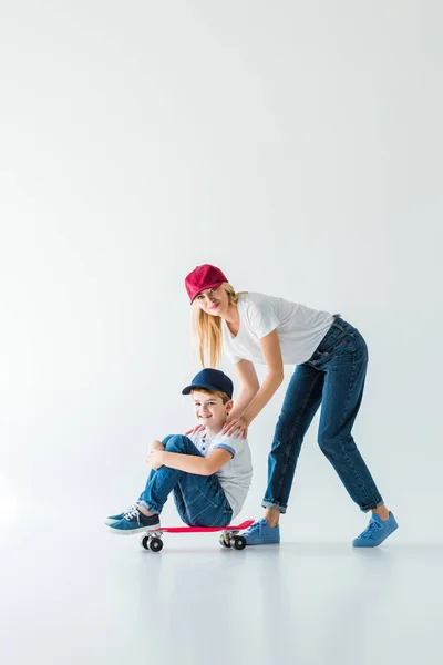 Счастливая мать в красной шапке толкает сына на коньках на белом — стоковое фото