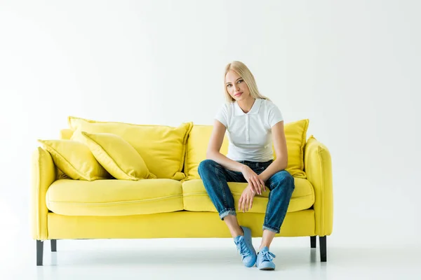 Attractive woman sitting on yellow sofa and looking at camera on white — Stock Photo