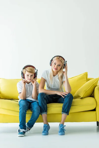 Alegre madre e hijo escuchando música con auriculares en sofá amarillo sobre blanco - foto de stock