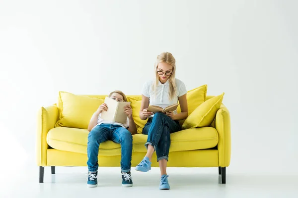 Attraktive Mutter und entzückender Sohn lesen Bücher auf gelbem Sofa auf weißem — Stockfoto