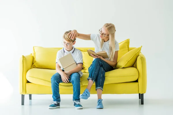 Mãe tocando cabelo filho enquanto ele lendo livro no sofá amarelo — Fotografia de Stock